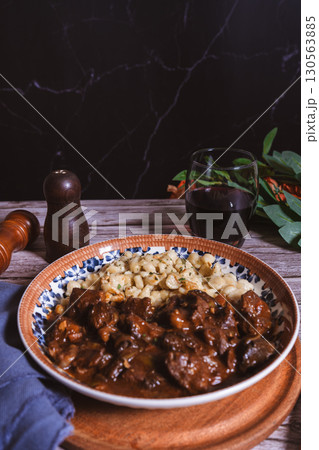 Hungarian goulash with spaetzle and red wine on rustic table setting 130563885