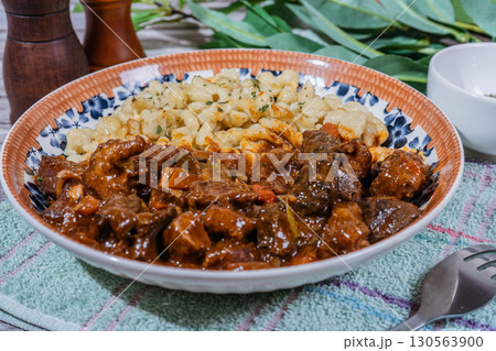 Delicious hungarian goulash with spaetzle, a traditional stew, resting on rustic table 130563900