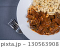 Delicious hungarian goulash with spaetzle on white plate resting on gray tablecloth with fork 130563908