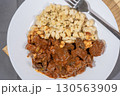 Delicious hungarian goulash with spaetzle garnished with parsley on white plate 130563909