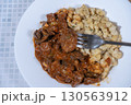 Fork taking a bite of beef goulash with spaetzle on white plate 130563912