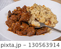 Fork picking up spaetzle from a plate of goulash and spaetzle 130563914