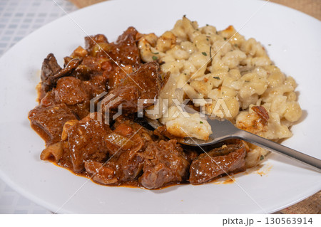 Fork picking up spaetzle from a plate of goulash and spaetzle 130563914
