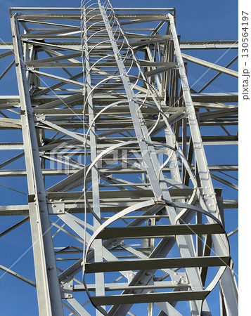 Electrical transmission tower showing detailed metal structure and ladder against clear blue sky 130564197