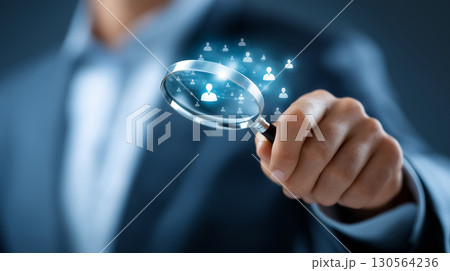 Person holds magnifying glass highlighting digital icons of people, signifying focus on customer relationship management. Professional environment with soft blue tones. 130564236