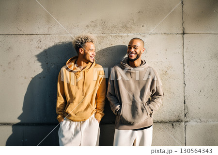 Two men are standing next to each other, smiling and wearing hoodies 130564343