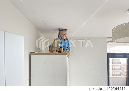 Cute young girl climbing on a high cabinet having fun 130564411