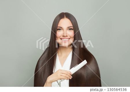 Studio portrait of woman brunette with long straight smooth hairstyle using hair straightener iron  130564536
