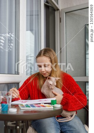 Beautiful young girl painting. Child and colorful paints and kitten at home. Childhood, hobby Beautiful young girl painting. Child and colorful paints and kitten at home. Childhood, hobby 130564869