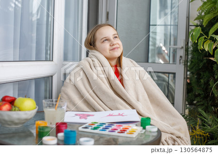 Joyful child in a warm fleece blanket relaxing on the balcony on cool spring day. Young girl at home Joyful child in a warm fleece blanket relaxing on the balcony on cool spring day. Young girl at home 130564875