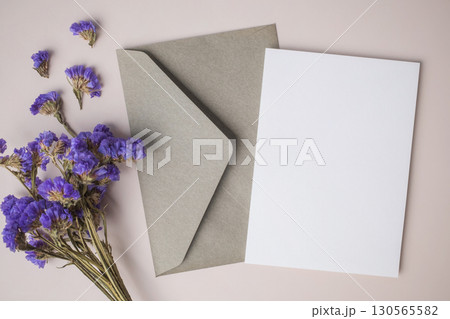 White blank greeting or invitation card with envelope and purple flower decoration on beige background. 130565582