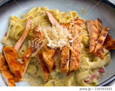 Close-up of pasta with grilled chicken and parmesan in creamy sauce. Gourmet cuisine, indulgence, and food lifestyle in restaurant dining culture. 130565883