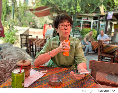 Woman sitting at cafe table drinking soda with straw. Lifestyle, leisure, and hospitality reflecting social interaction, cultural atmosphere, and outdoor relaxation. Woman sitting at cafe table drinking soda with straw. Lifestyle, leisure, and hospitality reflecting social interaction, cultural atmosphere, and outdoor relaxation. 130566172