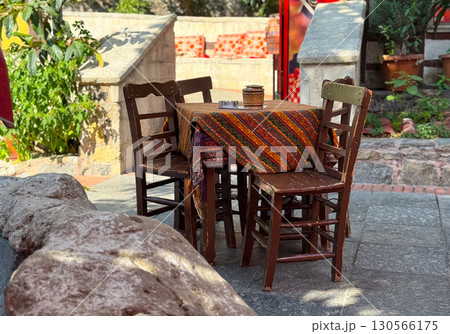Wooden chairs and table with patterned cloth in outdoor cafe. Tradition, culture, and rustic hospitality illustrating artisan craft, decoration, and lifestyle atmosphere. Wooden chairs and table with patterned cloth in outdoor cafe. Tradition, culture, and rustic hospitality illustrating artisan craft, decoration, and lifestyle atmosphere. 130566175