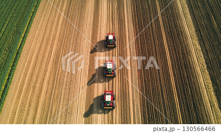 Aerial view of tractors working in parallel rows on large farm, showcasing agricultural activity and open space 130566466