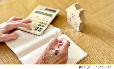 家小物の前でノートを広げて電卓を打つ高齢女性の手元 130567912