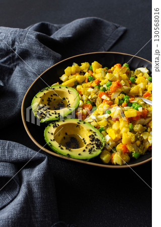 Healthy salad includes boiled egg, tender chicken breast, diced potatoes, vibrant carrots, fresh green peas, and creamy avocado topped with sesame seeds and drizzled with olive oil 130568016