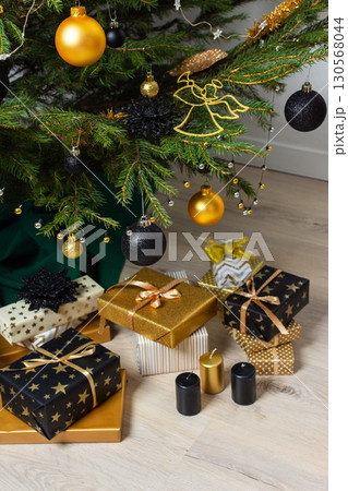 A festive scene featuring gold and black gift boxes, surrounded by shimmering candlelight and stylish decorations under a beautifully decorated Christmas tree, exuding elegance and charm A festive scene featuring gold and black gift boxes, surrounded by shimmering candlelight and stylish decorations under a beautifully decorated Christmas tree, exuding elegance and charm 130568044