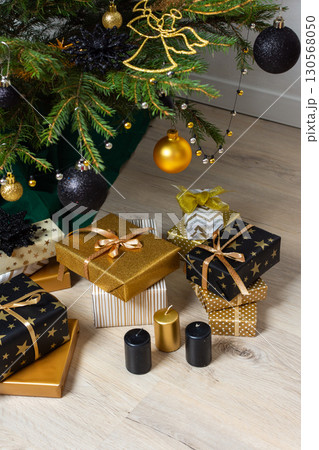 A festive scene featuring gold and black gift boxes, surrounded by shimmering candlelight and stylish decorations under a beautifully decorated Christmas tree, exuding elegance and charm A festive scene featuring gold and black gift boxes, surrounded by shimmering candlelight and stylish decorations under a beautifully decorated Christmas tree, exuding elegance and charm 130568050