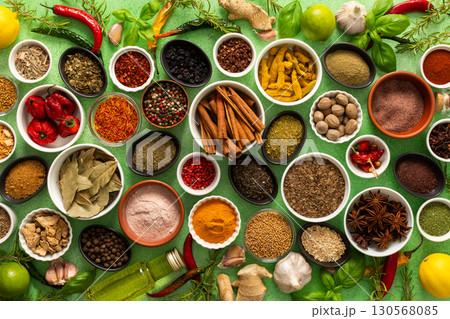A colorful assortment of fresh, fragrant spices and herbs displayed on a soft green background, capturing a vibrant culinary essence 130568085