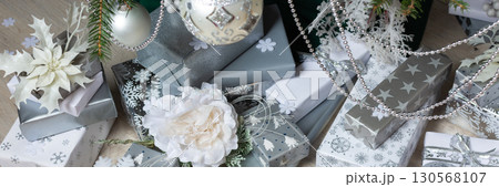 A cozy holiday scene featuring metallic steel-colored gift boxes, flickering candles, and intricate decorations under the Christmas tree, exuding warmth and seasonal cheer, banner A cozy holiday scene featuring metallic steel-colored gift boxes, flickering candles, and intricate decorations under the Christmas tree, exuding warmth and seasonal cheer, banner 130568107