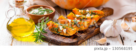 Pumpkin slices, roasted to a golden brown, are artfully placed on a rustic wooden board. Fresh herbs add a touch of color, creating a warm, inviting autumn atmosphere, banner 130568195