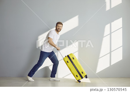 Young happy bearded man with suitcase is going on summer holiday isolated on grey background. Young happy bearded man with suitcase is going on summer holiday isolated on grey background. 130570545