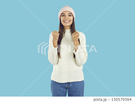 Overjoyed happy brunette girl in pink hat and white sweater showing yes gesture on blue background. 130570564