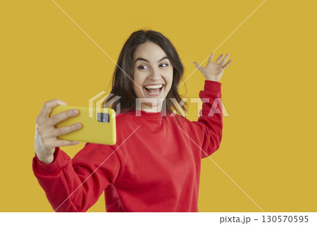 Happy attractive woman in red sweatshirt on yellow background taking selfie on smartphone. Happy attractive woman in red sweatshirt on yellow background taking selfie on smartphone. 130570595