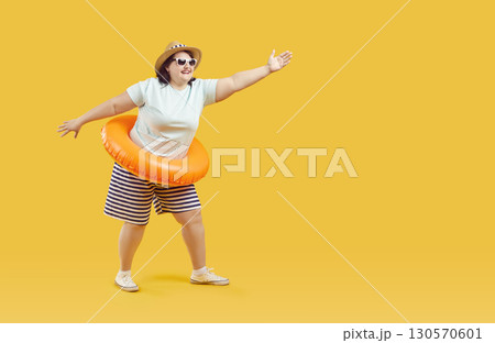 Funny fat woman in sunglasses in rubber ring pointing to the side with hand on yellow background. Funny fat woman in sunglasses in rubber ring pointing to the side with hand on yellow background. 130570601