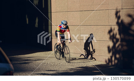Cyclist riding road bike in shaded urban street with dramatic shadow on wall 130570899