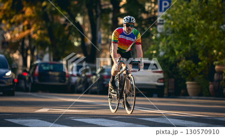 Cyclist in colorful jersey riding road bike on city street in sunset light Cyclist in colorful jersey riding road bike on city street in sunset light 130570910