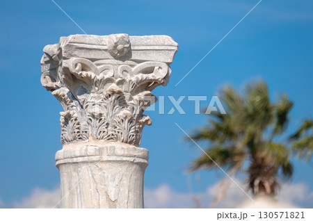 Corinthian capital of Kourion archaeological site in Cyprus with blurred palm tree and blue sky 130571821
