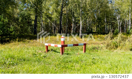 Red white striped boundary stake marking forest land limits in a grassy forest area, surrounded by vegetation. Ideal for surveying, property. 130572437