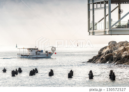 Traditional Cypriot fishing boat sailing near modern building and breakwater on sea. Limassol, Cyprus 130572527