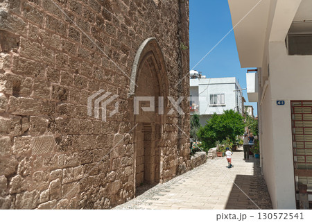 Tourists walking narrow stone-walled street with pointed arch, revealing medieval architectural heritage of Famagusta's historic urban landscape. Cyprus 130572541