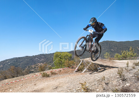 Mountain biker soaring through the air while performing a jump on a mountain bike under a bright blue sky on a sunny summer day 130572559