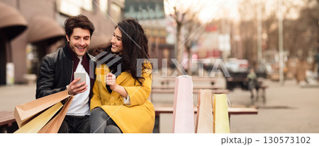 Happy shopaholics sitting on bench and shopping online with credit card and phone, panorama with copy space Happy shopaholics sitting on bench and shopping online with credit card and phone, panorama with copy space 130573102
