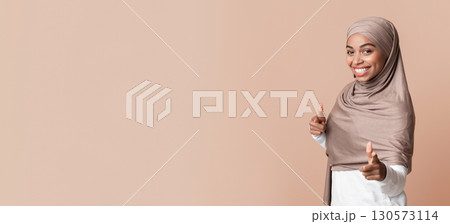 Gotcha. Smiling Black Muslim Woman In Headscarf Pointing Fingers At Camera, Posing Over Yellow Background In Studio, Free Space Gotcha. Smiling Black Muslim Woman In Headscarf Pointing Fingers At Camera, Posing Over Yellow Background In Studio, Free Space 130573114