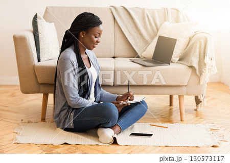 Exam preparation. Black female student taking notes while watching webinar on laptop, studying at home Exam preparation. Black female student taking notes while watching webinar on laptop, studying at home 130573117