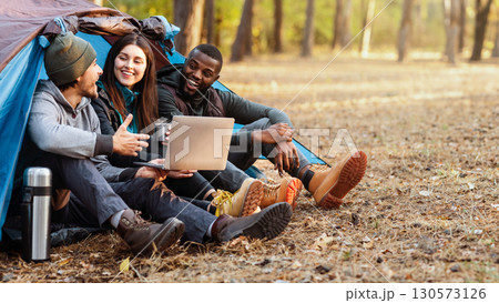 Cheerful international friends sitting in tent, discussing route, using laptop, free space 130573126