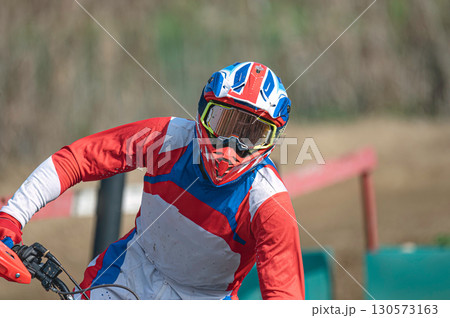 Motocross rider wearing helmet and goggles racing on dirt track 130573163