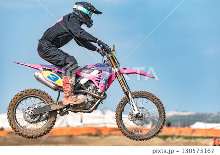 Motocross rider wearing pink and black protective gear jumping during a race on a pink dirt bike 130573167