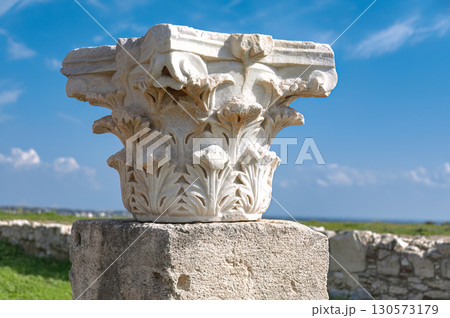 White marble corinthian capital with acanthus leaves decorations standing on a stone base at Kourion archaeological site, against blue sky. Cyprus White marble corinthian capital with acanthus leaves decorations standing on a stone base at Kourion archaeological site, against blue sky. Cyprus 130573179