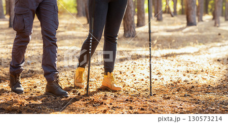 Legs of hikers man and woman walking by forest, girl using walking sticks, cropped, copy space 130573214