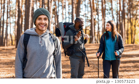 Happy guy backpacker smiling over his talking friends, hiking by forest 130573225
