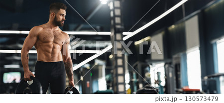 Young muscular athlete exercising with barbell weights in gym interior, empty space, panorama 130573479