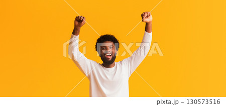 Cheerful african american man screaming Yes and raising clenched fists in the air, feeling excited, orange studio background, panorama with copy space 130573516