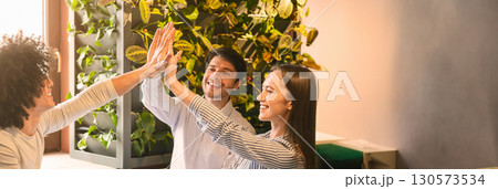 Excited multiethnic team giving each other high five, celebrating success while working together on project at cafe, copy space 130573534