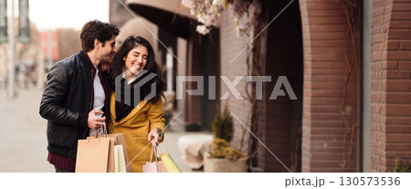 A happy couple strolls through a vibrant outdoor market, holding shopping bags while smiling and enjoying each other's company, copy space A happy couple strolls through a vibrant outdoor market, holding shopping bags while smiling and enjoying each other's company, copy space 130573536